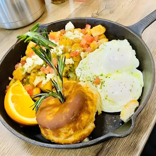 Chops & Eggs breakfast skillet with potatoes, poached eggs, a pastry, and an orange slice.