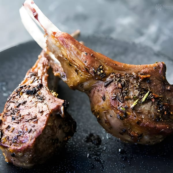 Two perfectly cooked lamb chops, seasoned with herbs and spices, resting on a dark plate.