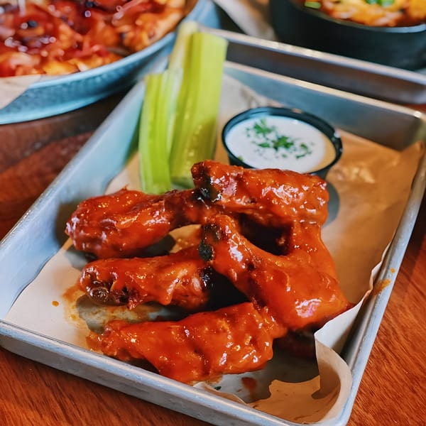 Buffalo chicken wings with celery sticks and ranch dressing on a metal tray.