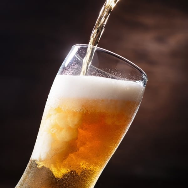 Golden beer being poured into a tall glass, creating a frothy white head.